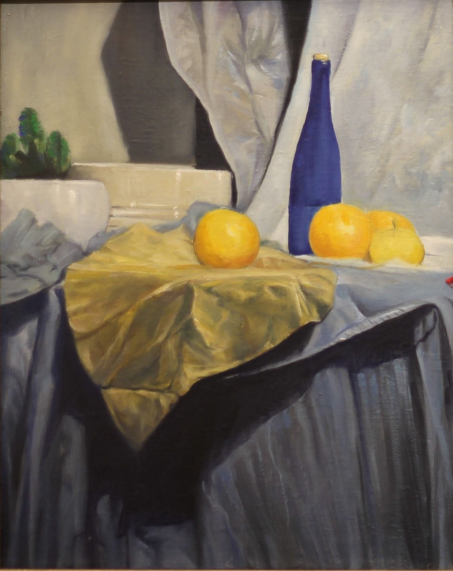 Na stole przykrytym szarą i żółtą tkaniną leżą cztery żółte owoce, wśród nich niebieska butelka
